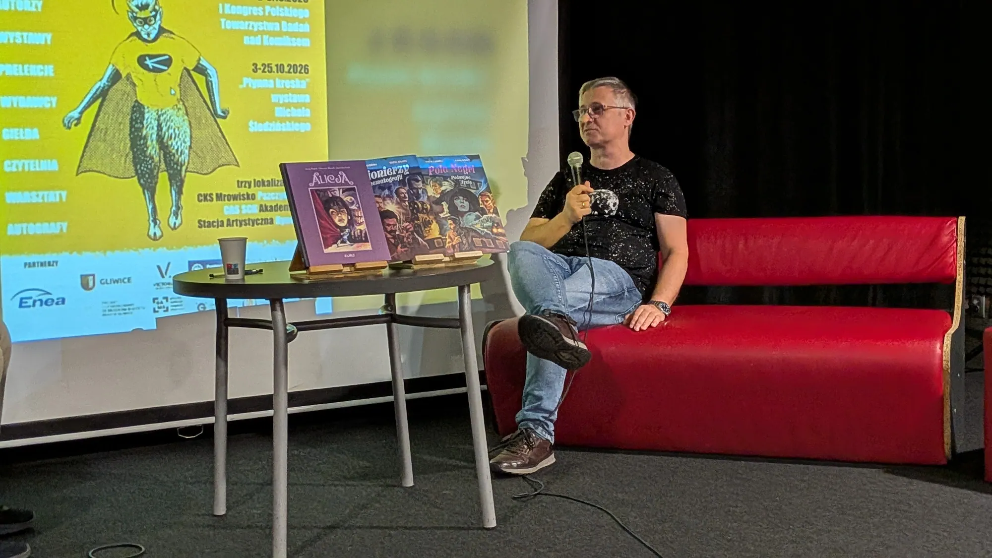 Rafał Szłapa na kanapie z mikrofonem opowiada o komiksach na GIK 5